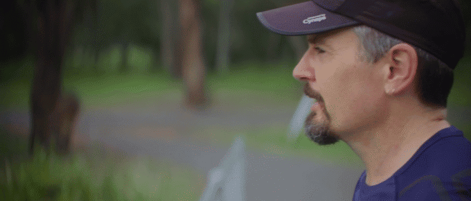 A man wearing a black cap and blue shirt stands outdoors, looking to the right, with greenery and trees in the blurred background—perhaps reflecting on recent projects or media appearances.