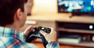 A person wearing a plaid shirt enjoys a video game with a controller, playing on a television screen in a cozy living room setting.