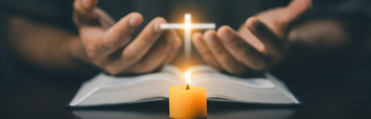 Person holding a glowing cross above an open book with a lit candle in front, suggesting a scene of prayer or meditation. This serene setting beautifully embodies meditation techniques, inviting reflection and spiritual connection.