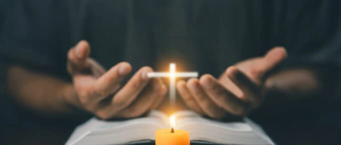 Person holding a glowing cross above an open book with a lit candle in front, suggesting a scene of prayer or meditation. This serene setting beautifully embodies meditation techniques, inviting reflection and spiritual connection.