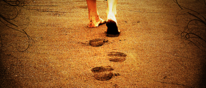 Barefoot man walking away on sandy ground, leaving a visible trail of footprints behind him—a quiet expression of masculinity in motion.