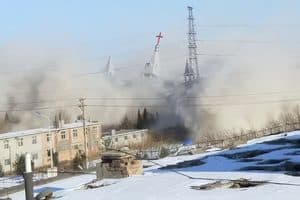 A dense cloud of smoke obscures a cityscape, reflecting the city’s profound suffering as only the spires of a church and a utility tower rise above the debris.