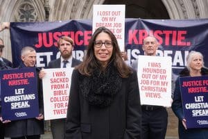 A woman stands with resilience in front of protesters holding signs about being fired for their Christian views and seeking justice for Kristie.