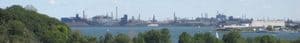 A large industrial steel plant stands on the shore, a testament to resilience, overlooking sailboats on the water.